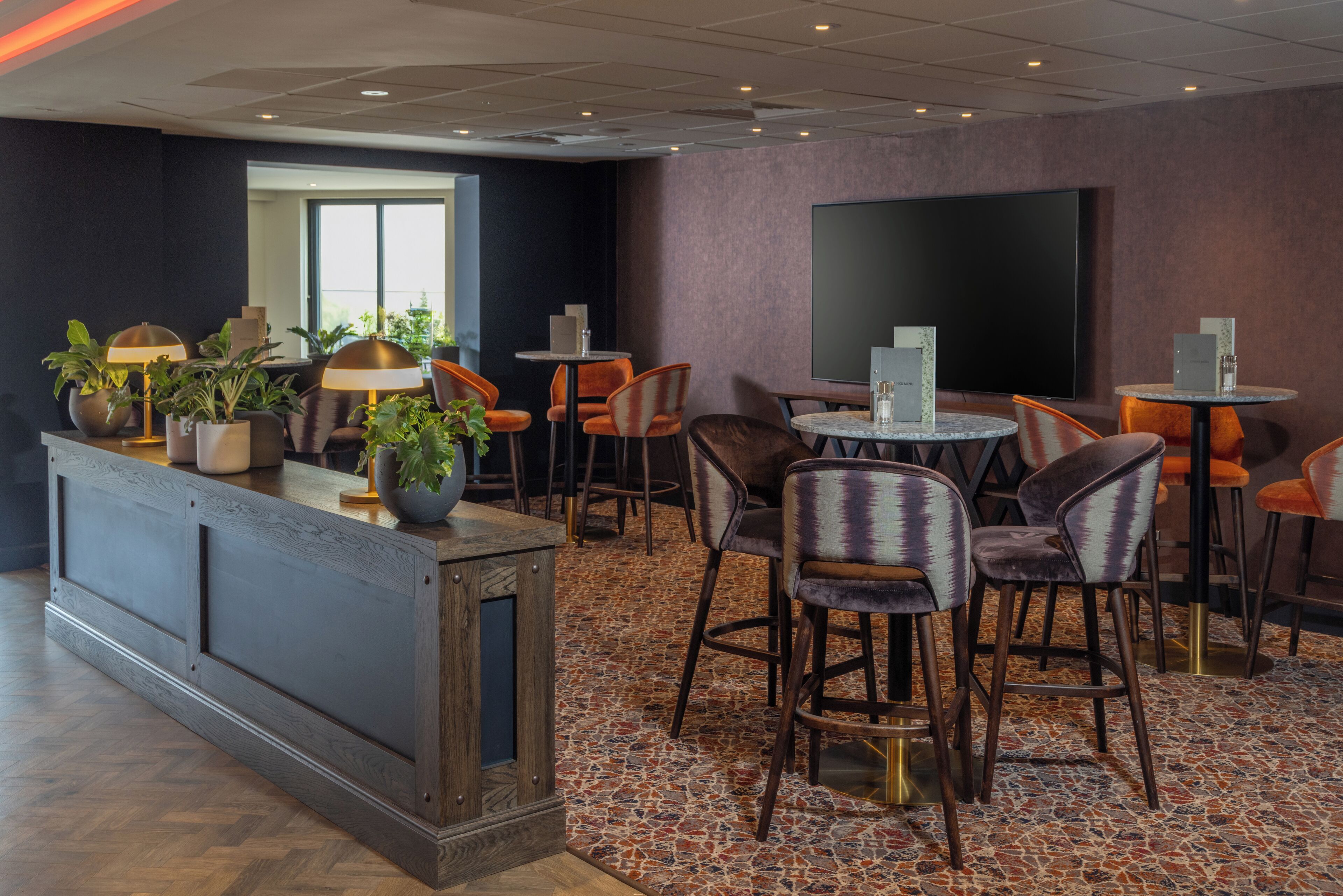 Un hall d’hôtel moderne doté d’un comptoir d’accueil, de plusieurs espaces salon et d’un grand téléviseur à écran plat fixé au mur.