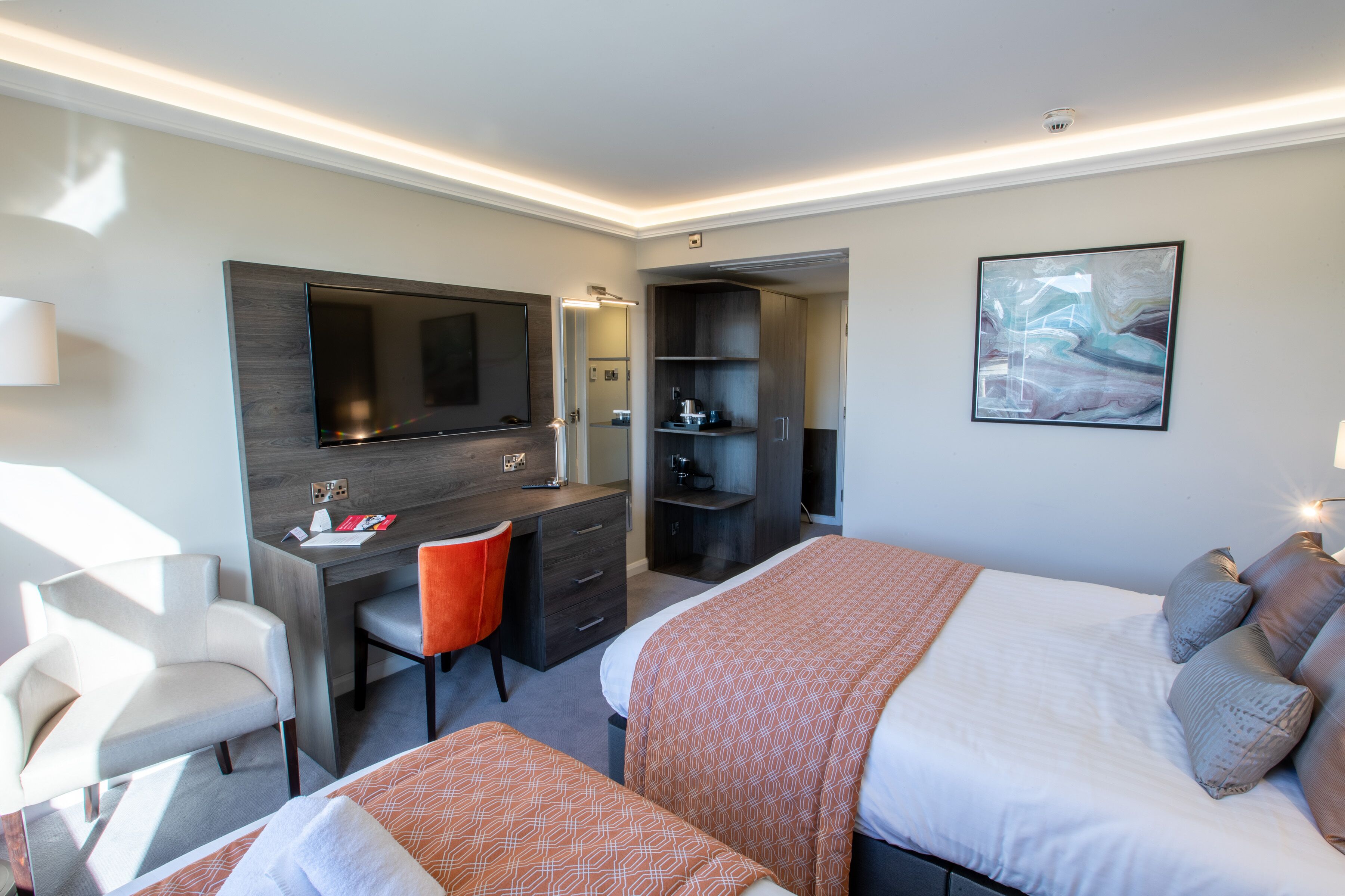 A hotel room with a bed, a desk, a chair, a TV, and a painting on the wall.