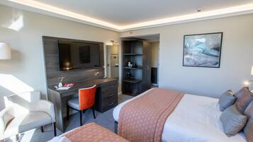 Quarto de hotel com cama, escrivaninha, cadeira, televisão e um quadro na parede.