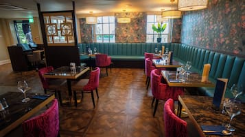 A restaurant with booths, red upholstered chairs, and a herringbone wood floor.