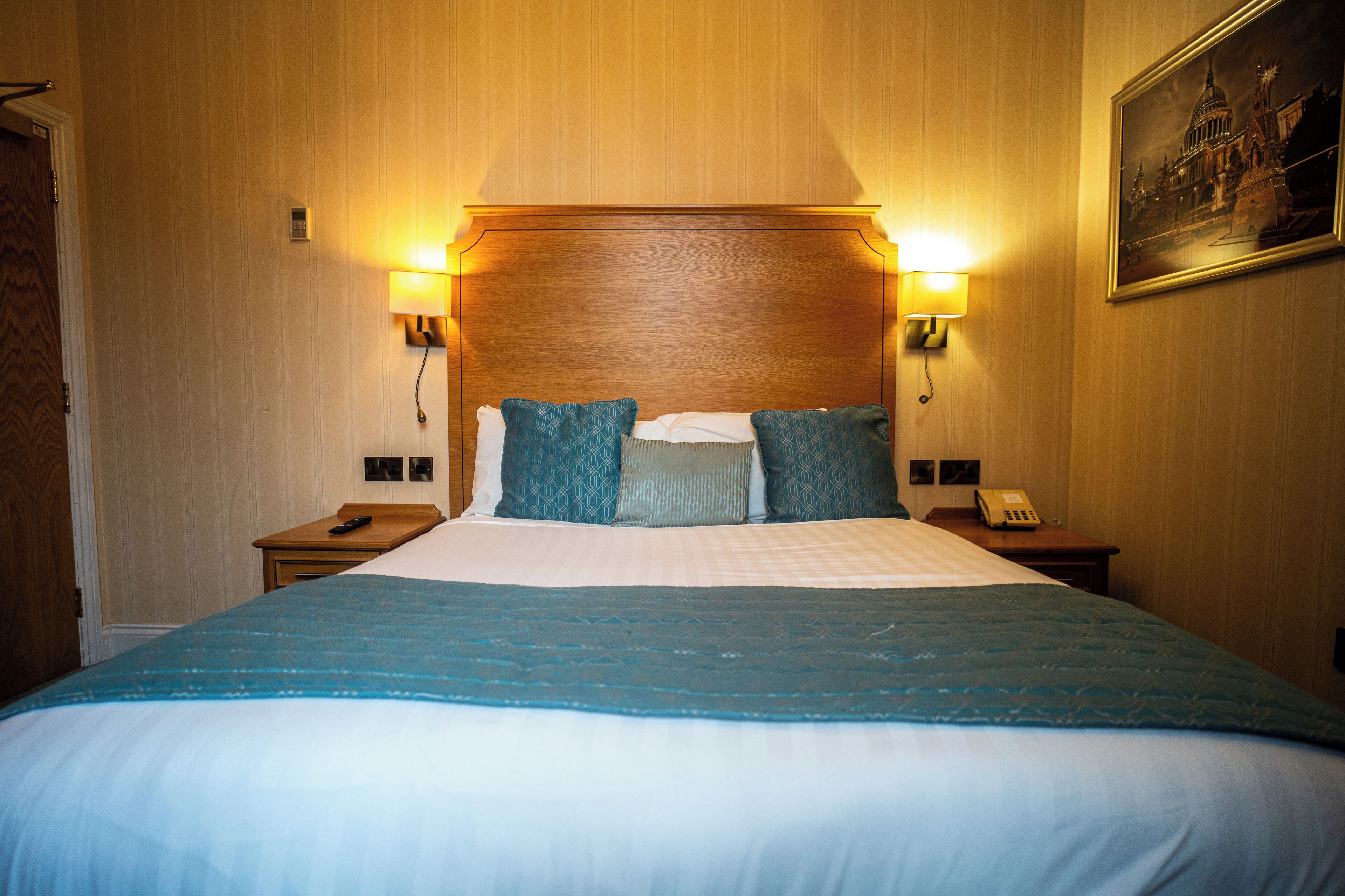 A hotel room with a large bed, two bedside lamps, a nightstand with a telephone, and a framed picture on the wall.