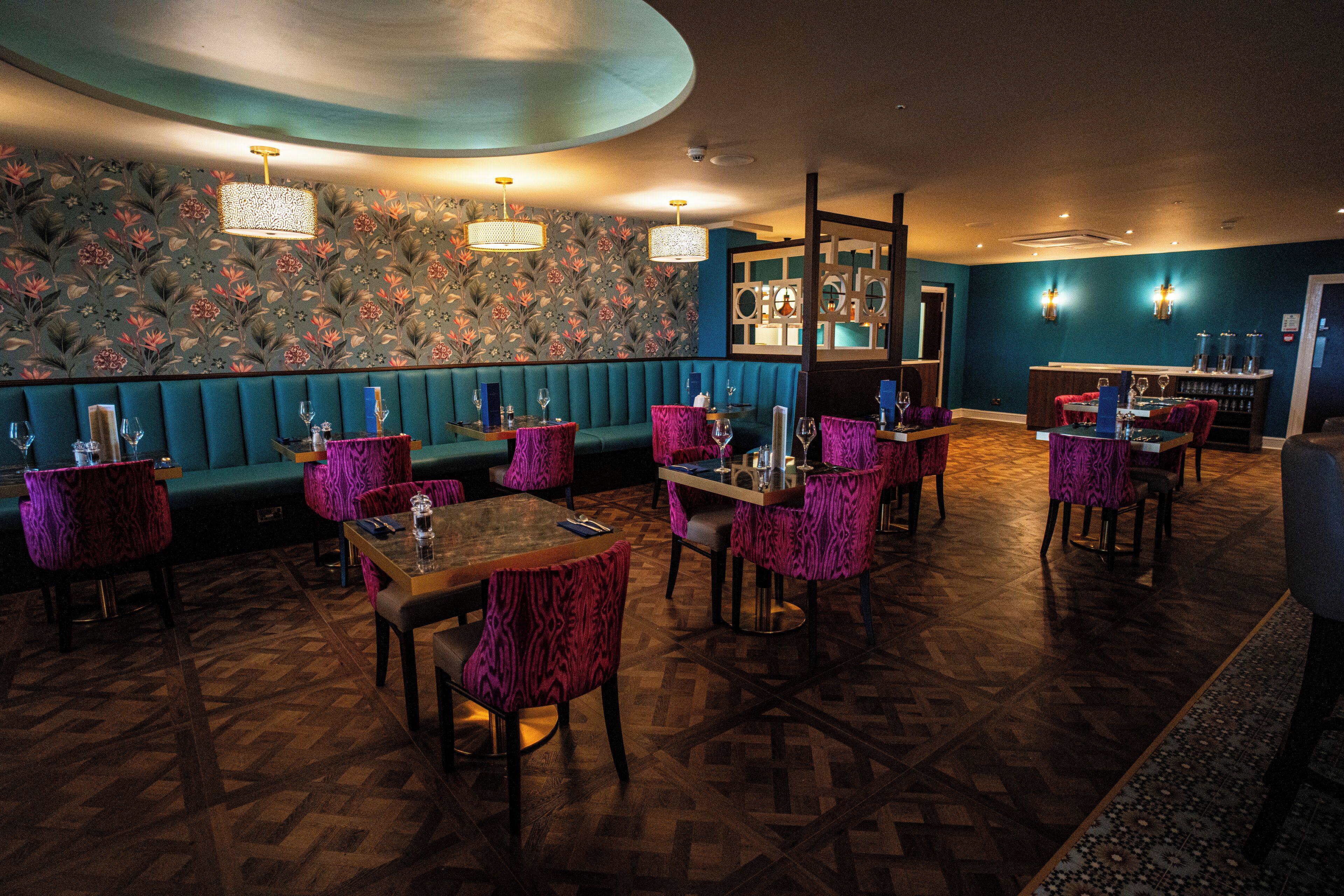 A restaurant with teal booths, purple upholstered chairs, and a patterned floor.