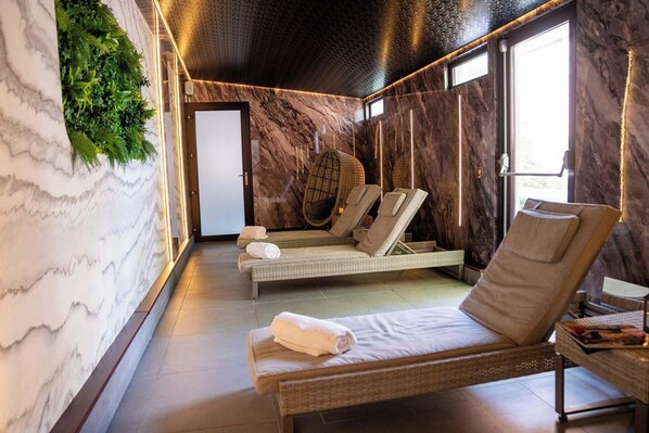 A spa room with a marble wall, a large window, and a seating area with loungers and a massage table. - Park Hall Hotel and Spa Wolverhampton (Wolverhampton)