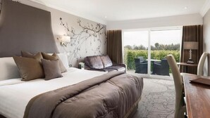 Una habitación de hotel moderna con una cama grande, un sofá, una mesa de comedor y vistas al exterior.