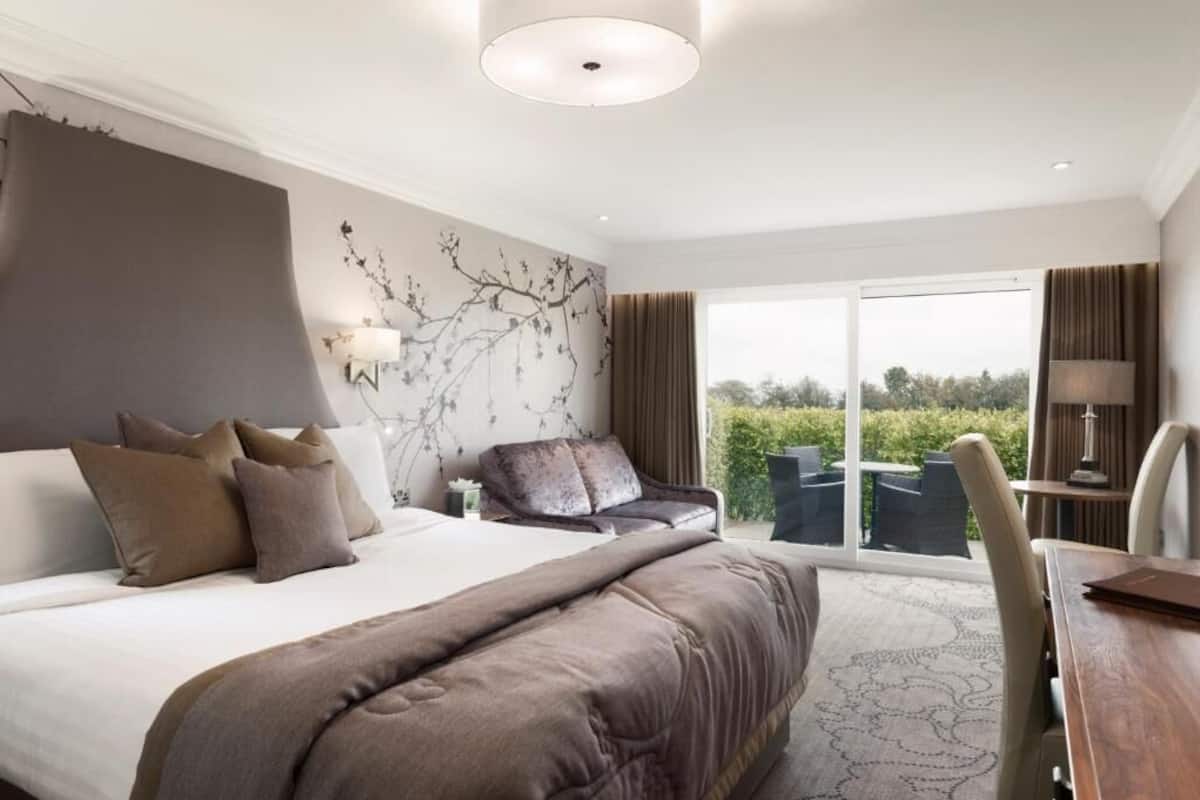 Una habitación de hotel moderna con una cama grande, un sofá, una mesa de comedor y vistas al exterior.