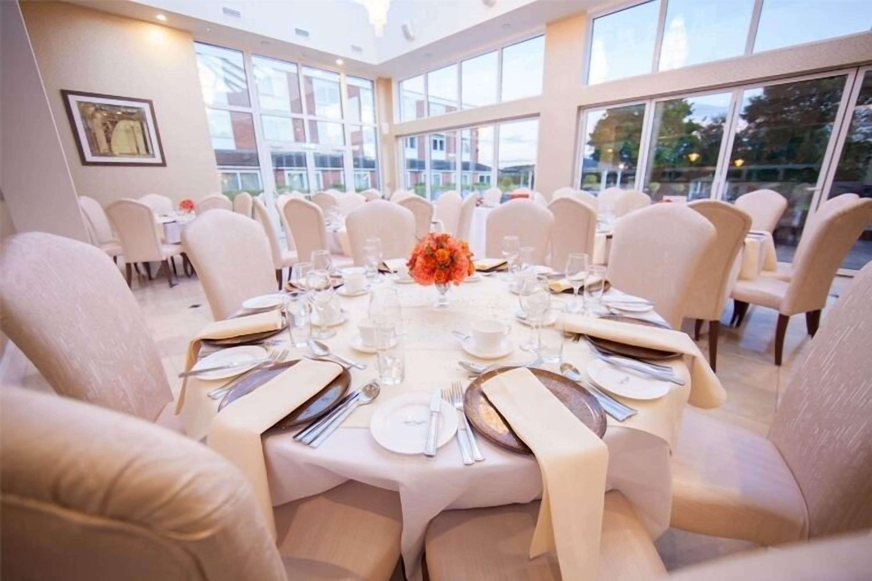 A formal dining room with round tables, white chairs, and a large window offering a view of the outside.