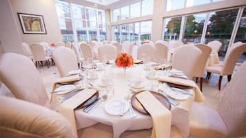 A formal dining room with round tables, white chairs, and a large window offering a view of the outside.