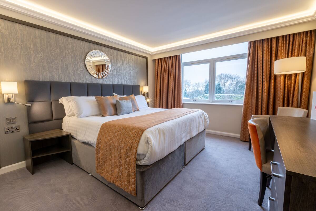 Una habitación de hotel moderna con una cama grande, una mesita de noche, un escritorio y una ventana con cortinas.