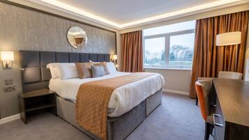 A modern hotel room with a large bed, a bedside table, a desk, and a window with curtains.