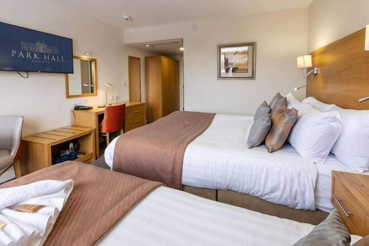 A hotel room with two beds, a desk, a chair, a TV, and a mirror.