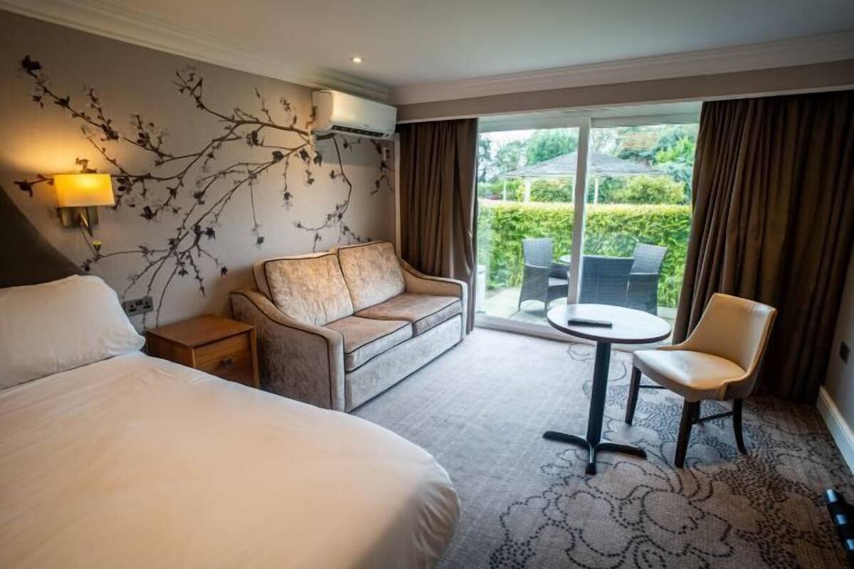 Habitación de hotel con cama, sofá, una mesita, una silla y vistas al exterior a través de una puerta corredera.