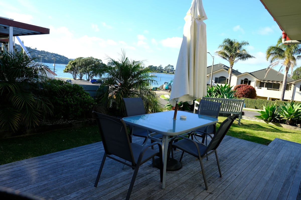 A patio with a table and chairs, overlooking a body of water and a hilly landscape.