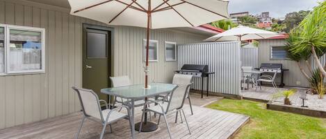 A patio with a glass table and chairs, a grill, and a covered umbrella.