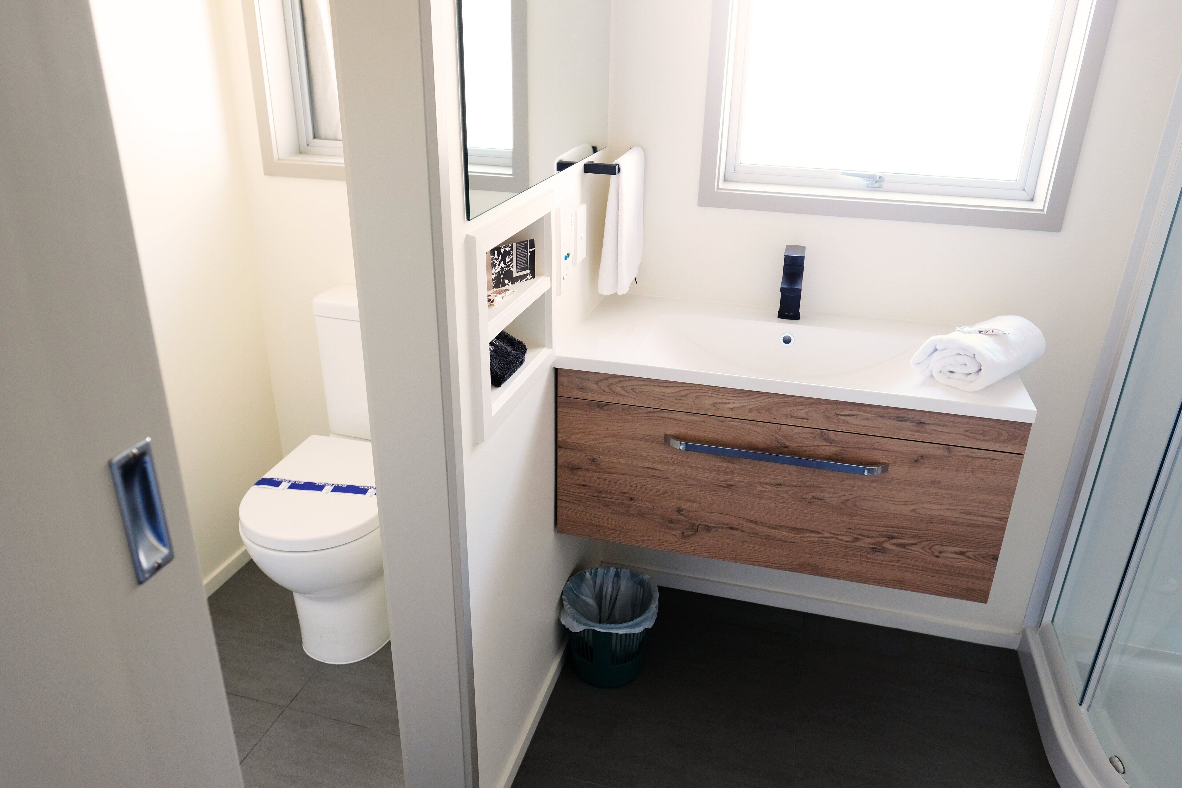 A modern bathroom with a white toilet, a wooden vanity with a towel, and a glass shower enclosure.