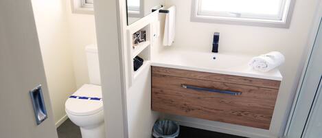 A modern bathroom with a white toilet, a wooden vanity with a towel, and a glass shower enclosure.