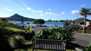 A coastal street with a bench, a road, and a view of the sea and a hill in the distance. - Tairua Shores (Tairua)