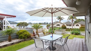 A covered patio with a table and chairs, overlooking a body of water and residential buildings. - Tairua Shores (Tairua)