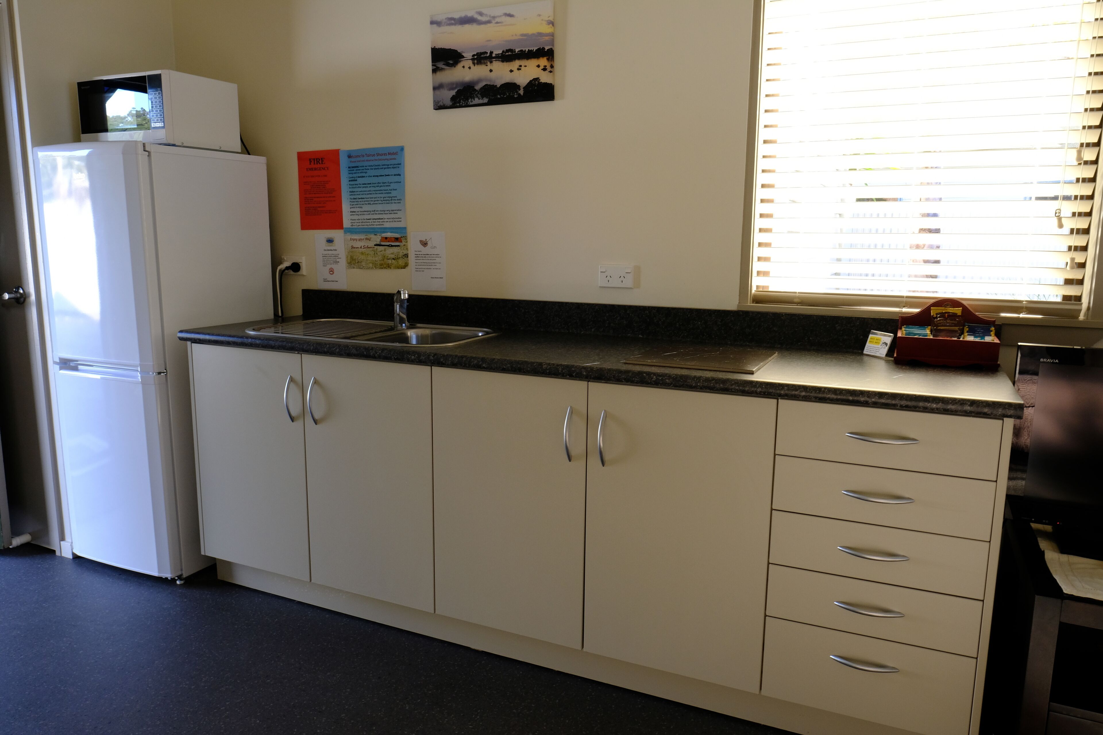 A kitchen with a refrigerator, sink, cabinets, and a window with blinds.