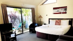 A hotel room with a bed, a TV, a chair, and a view of the outdoors. - Tairua Shores (Tairua)