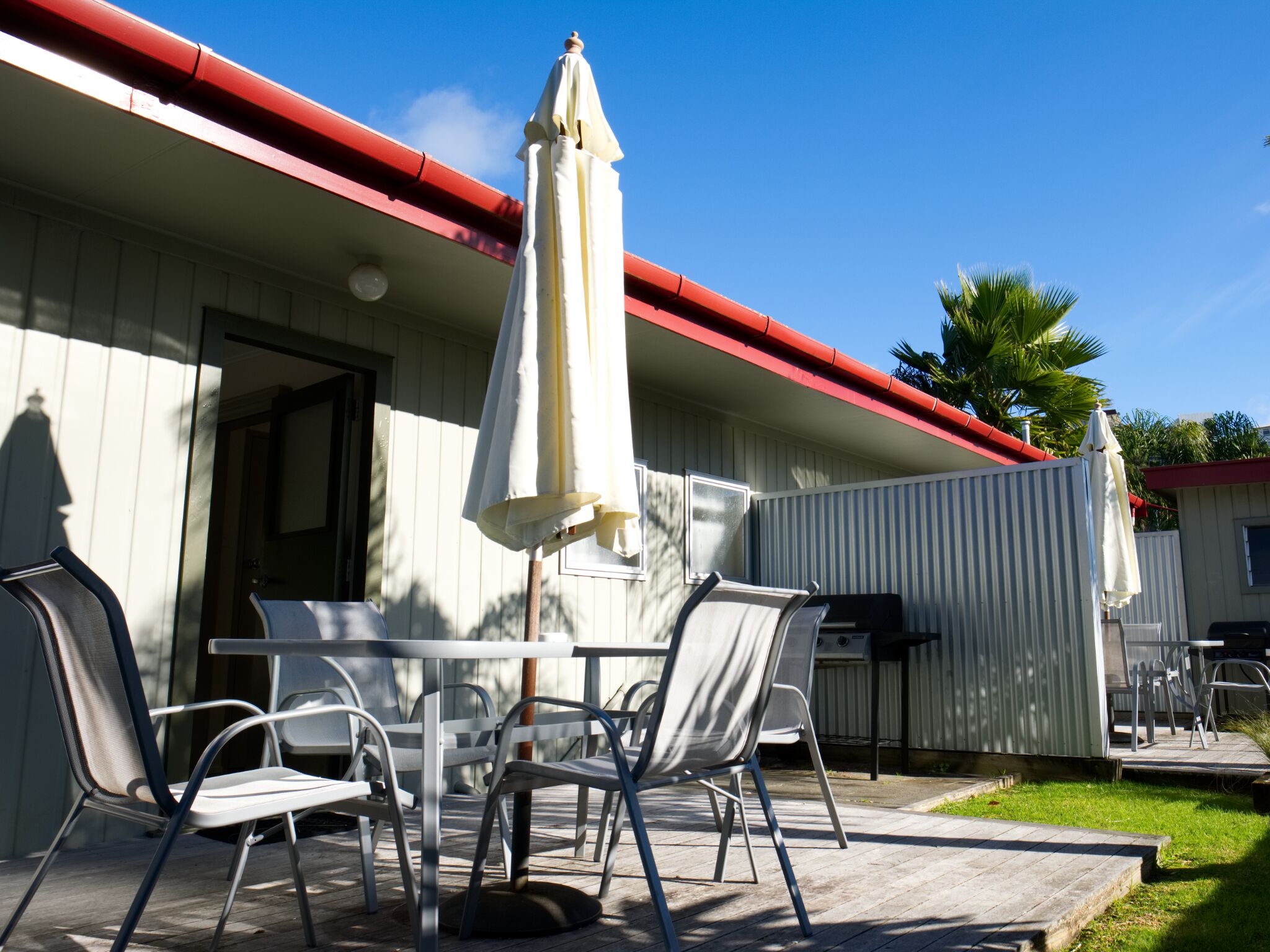 An outdoor patio with a table and chairs, a grill, and umbrellas.