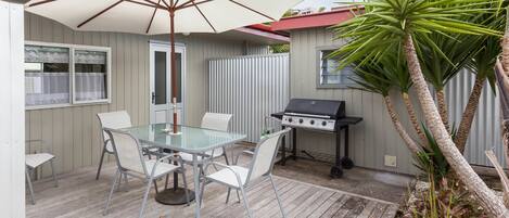 Eine Terrassenanlage im Freien mit Glastisch und Stühlen, einem Grill und einer Palme.