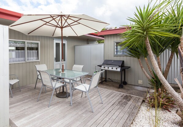 Un patio exterior con una mesa y sillas de vidrio, una parrilla y una palmera.