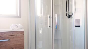 A glass-enclosed shower with a handheld showerhead, a wooden vanity with a towel, and a window above the vanity.