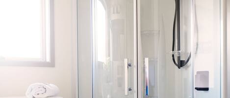 A glass-enclosed shower with a handheld showerhead, a wooden vanity with a towel, and a window above the vanity.