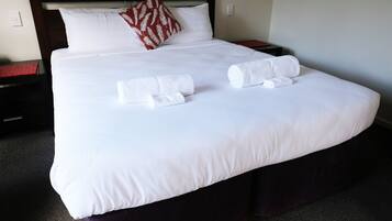 A neatly made bed with white linens, two rolled towels, and a decorative pillow.