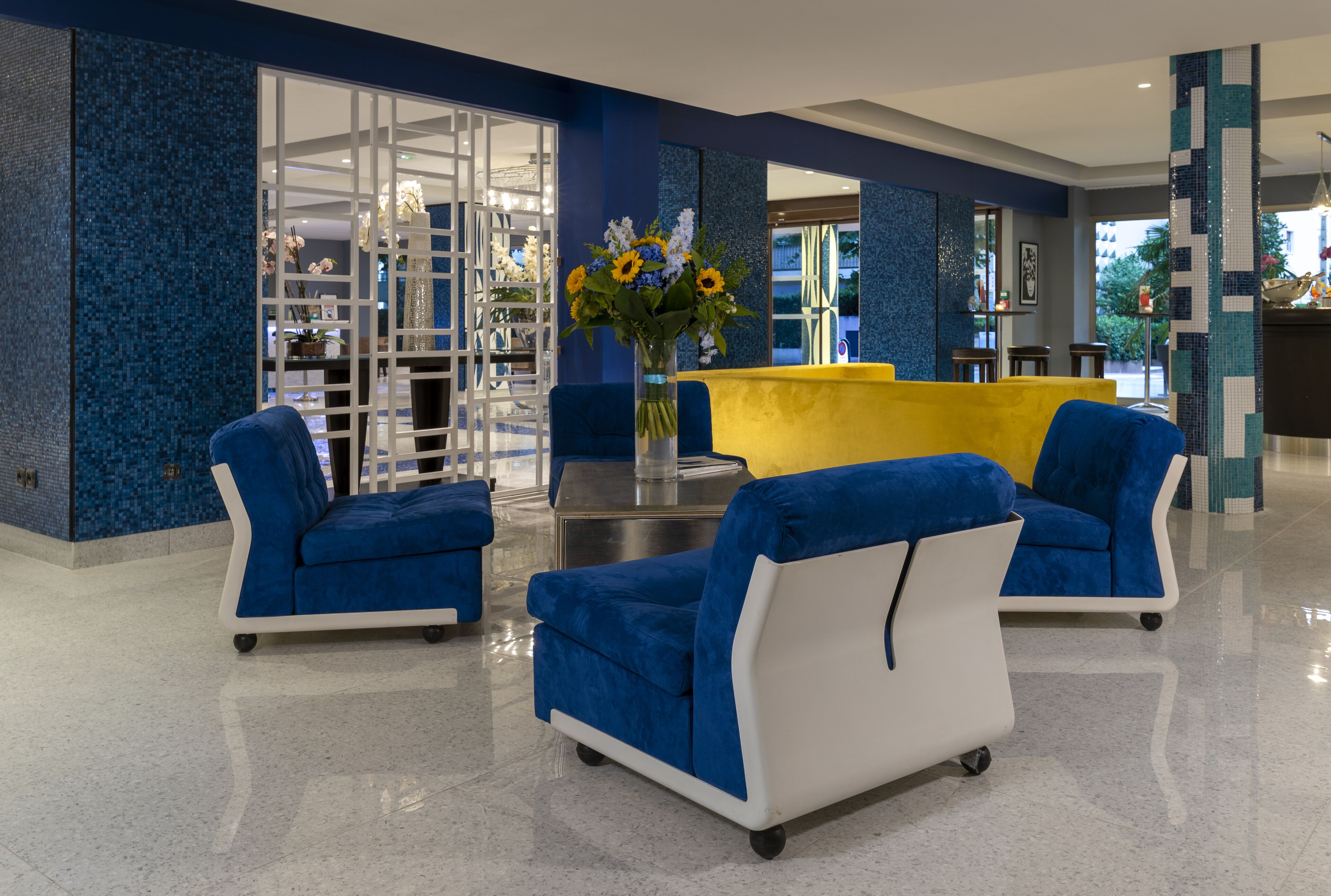 A lobby with blue and white armchairs, a yellow sofa, and a vase with flowers.
