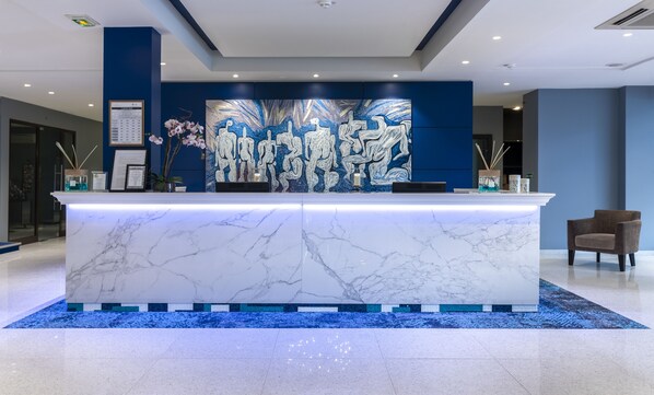 A marble reception desk with a blue and white abstract mural, a blue carpet, and a brown chair.