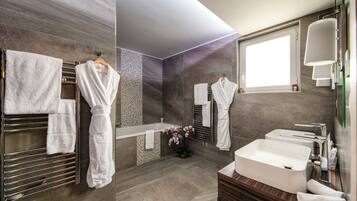 Ein modernes Badezimmer mit einer großen Badewanne, einem Waschbecken und einem Spiegel. Mehrere Handtücher und ein Topfpflanze sind vorhanden.