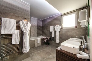 A modern bathroom with a large bathtub, a vanity with a sink, and a mirror. There are multiple towels and a potted plant.