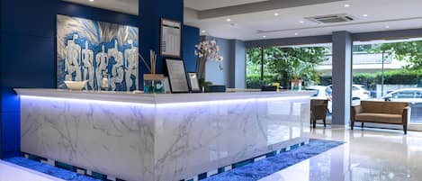 Una recepción moderna con una barra de mármol, un cuadro abstracto de gran tamaño y vistas al exterior.