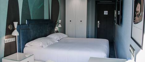 A hotel room with a bed, bedside table, lamp, and a desk with a chair.