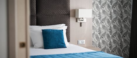 A hotel room with a bed, a headboard, a wall-mounted light, and patterned wallpaper.