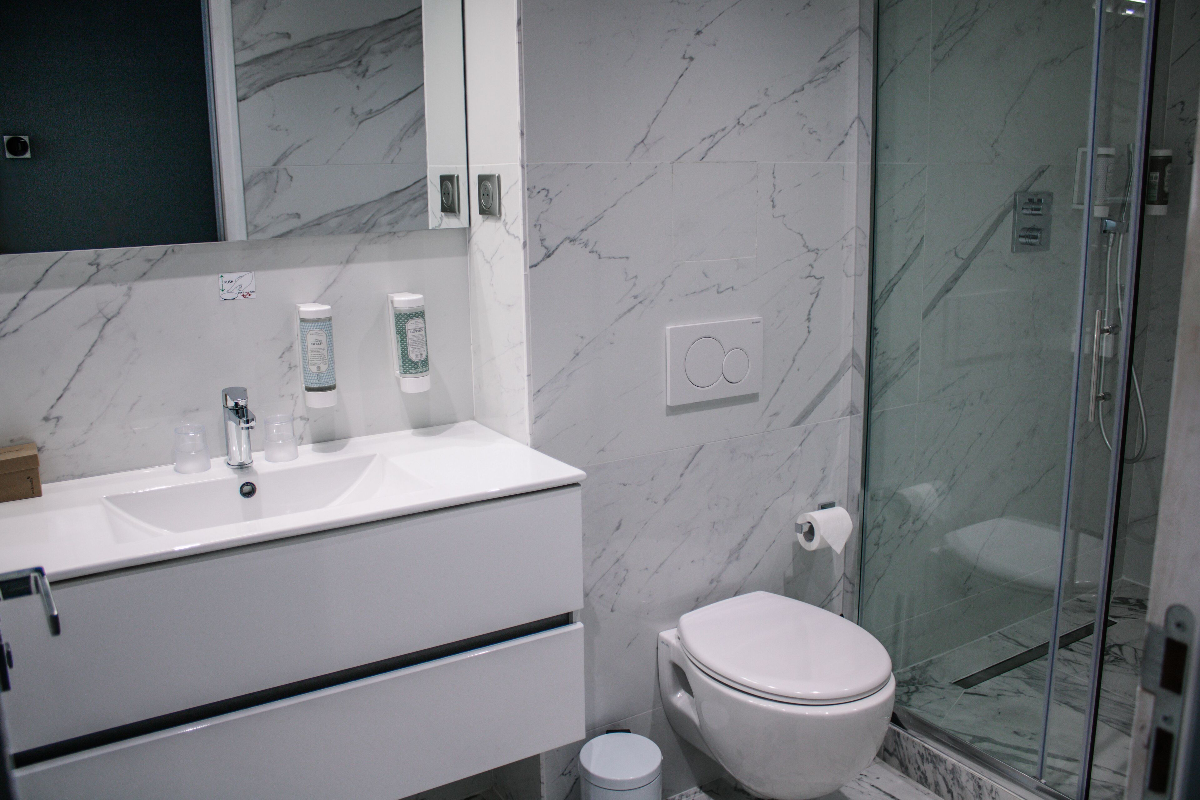 A modern bathroom with a marble sink, toilet, and glass shower enclosure.
