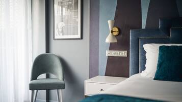 A hotel room with a bed, a chair, a nightstand, a wall-mounted lamp, and a framed picture.