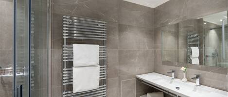 Ein modernes Badezimmer mit Duschabtrennung aus Glas, einem chromfarbenen Handtuchhalter und einem weißen Waschtisch mit Spiegel.