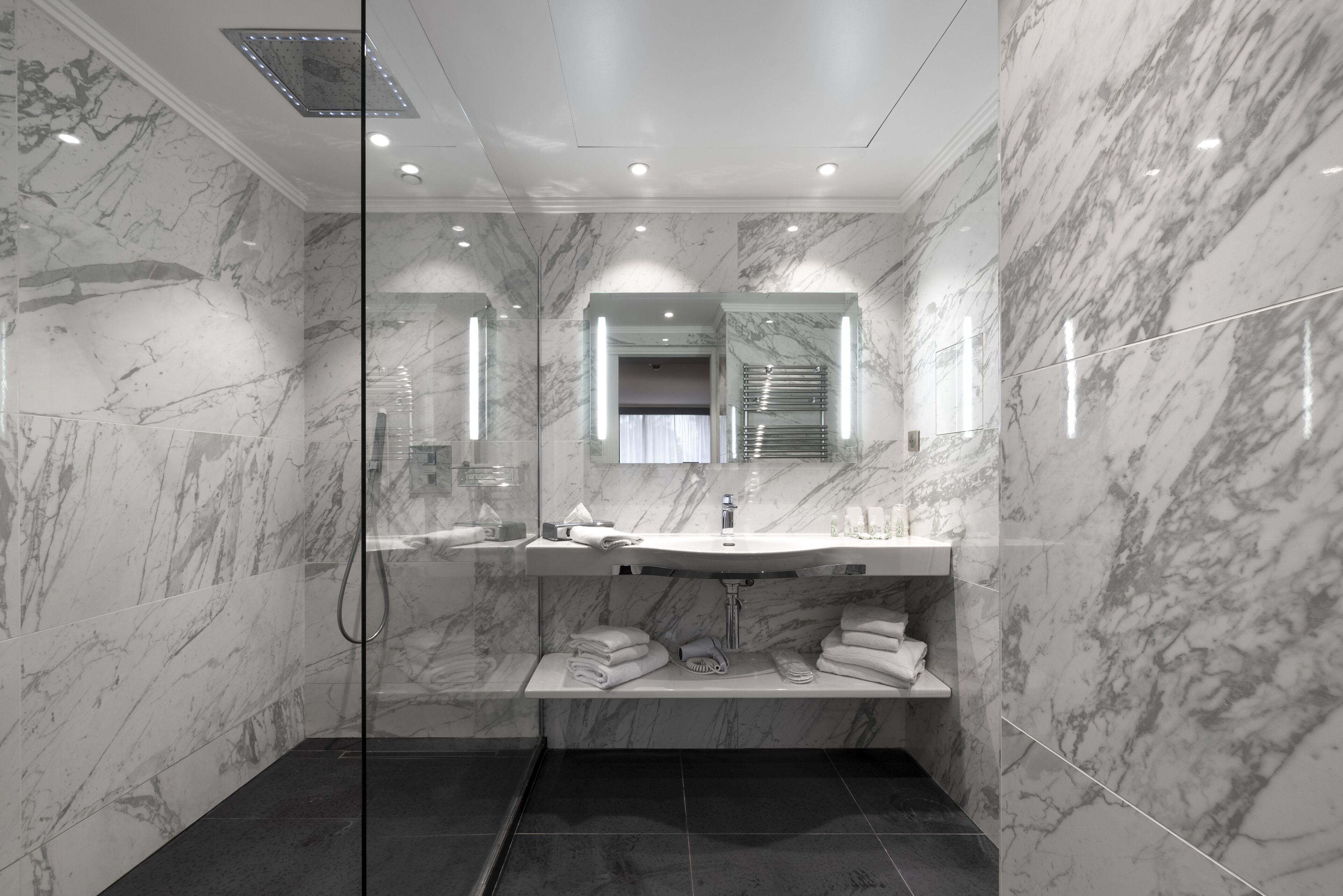 Een moderne badkamer met marmeren wanden, een douchecabine van glas en een wastafel met spiegel.