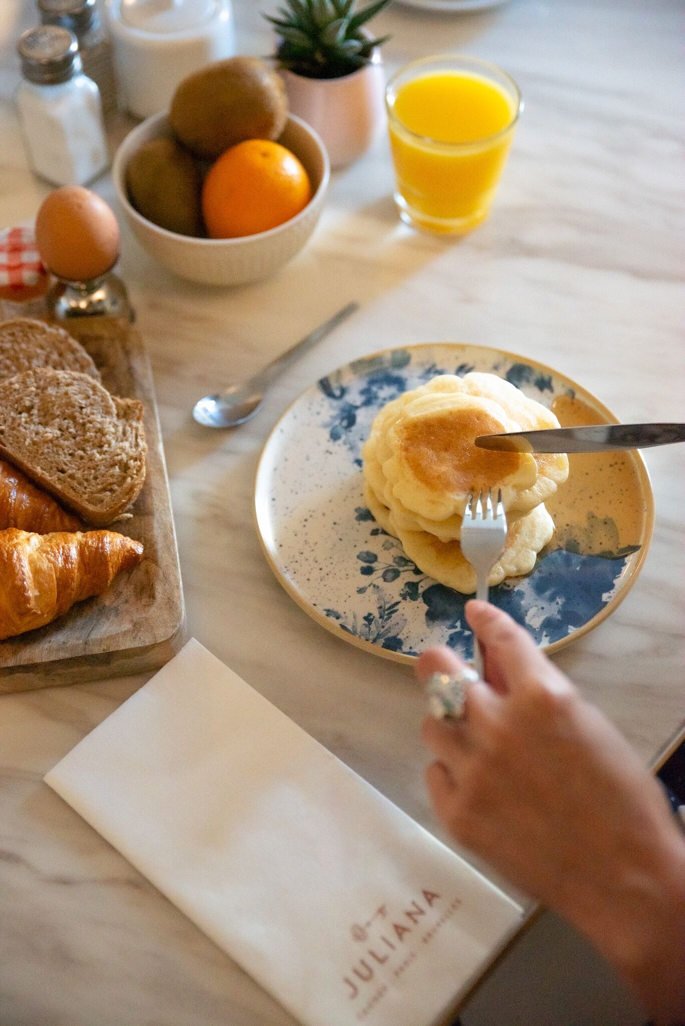 A breakfast setting with croissants, a bowl of fruit, a glass of orange juice, and a plate of scrambled eggs on a marble table.