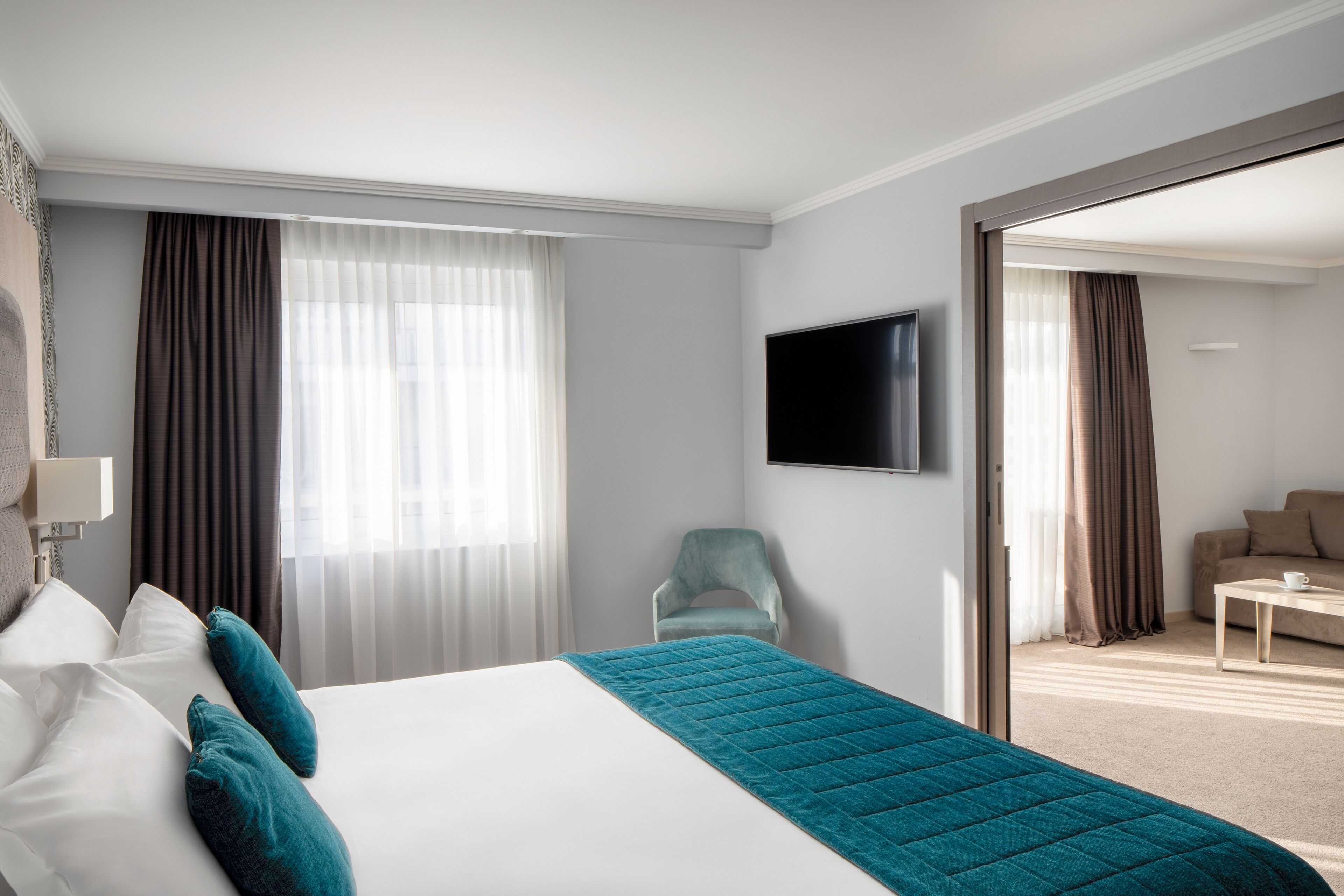 Quarto de hotel com uma cama grande, televisão, uma cadeira e vista para o exterior.