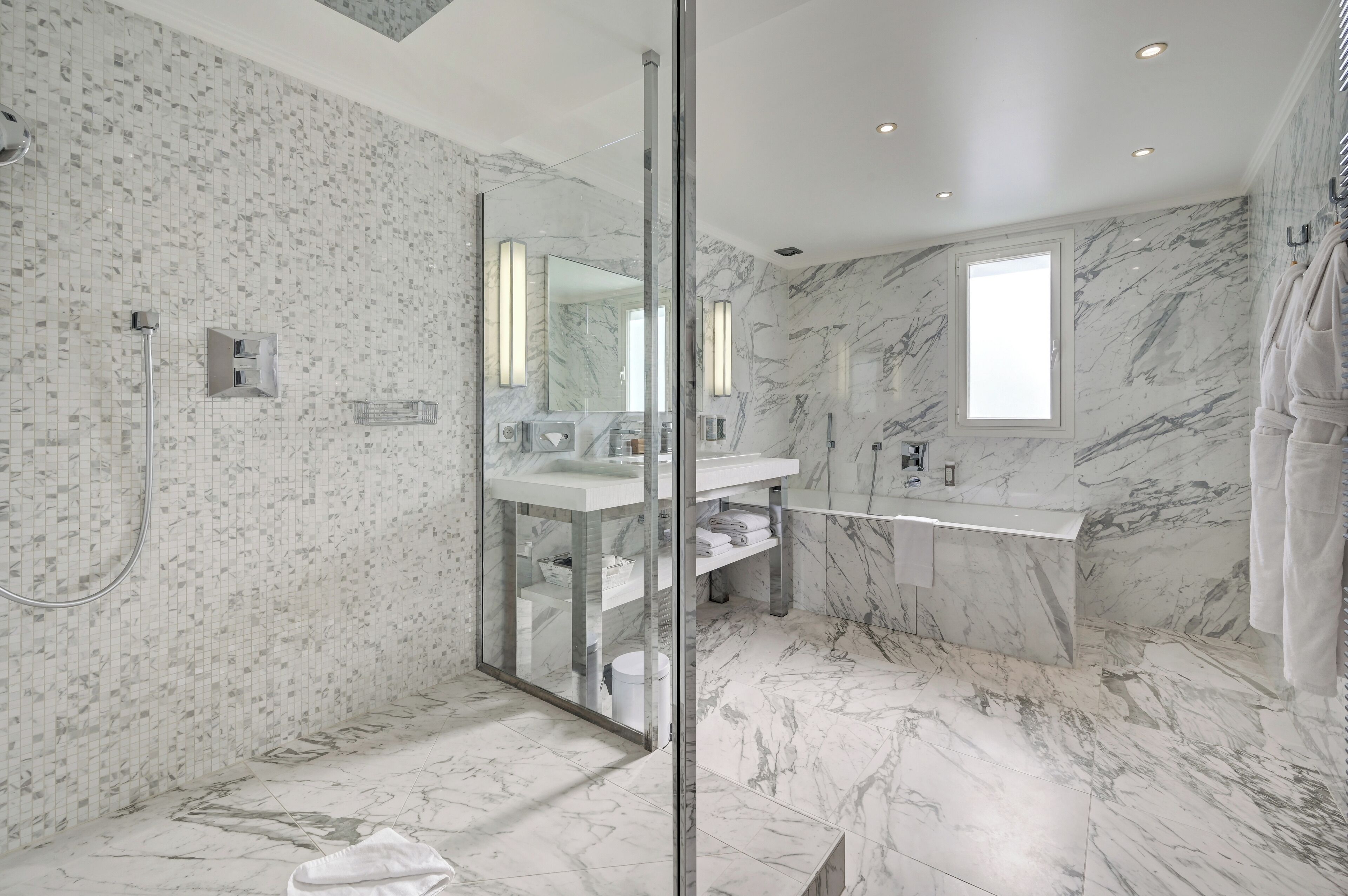 Une salle de bain moderne dotée d’une douche à parois de verre, de murs en marbre et d’un grand miroir.