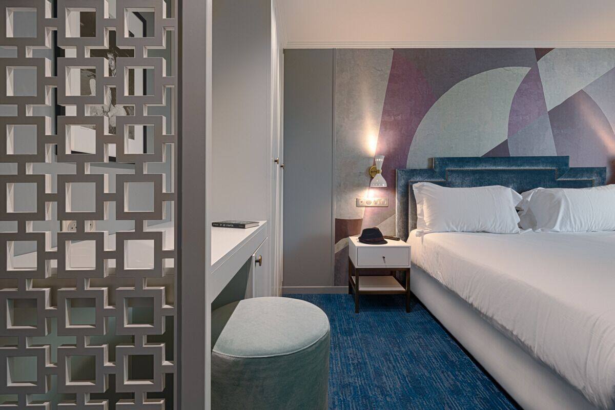A hotel room with a bed, nightstand, lamp, and a decorative wall.