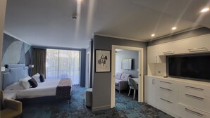 Una habitación de hotel moderna con cama, sofá, televisor y kitchenette.