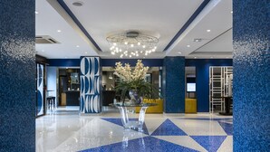 Un vestíbulo moderno con piso de baldosas geométricas, una mesa de vidrio central con un arreglo floral y una lámpara de araña contemporánea.