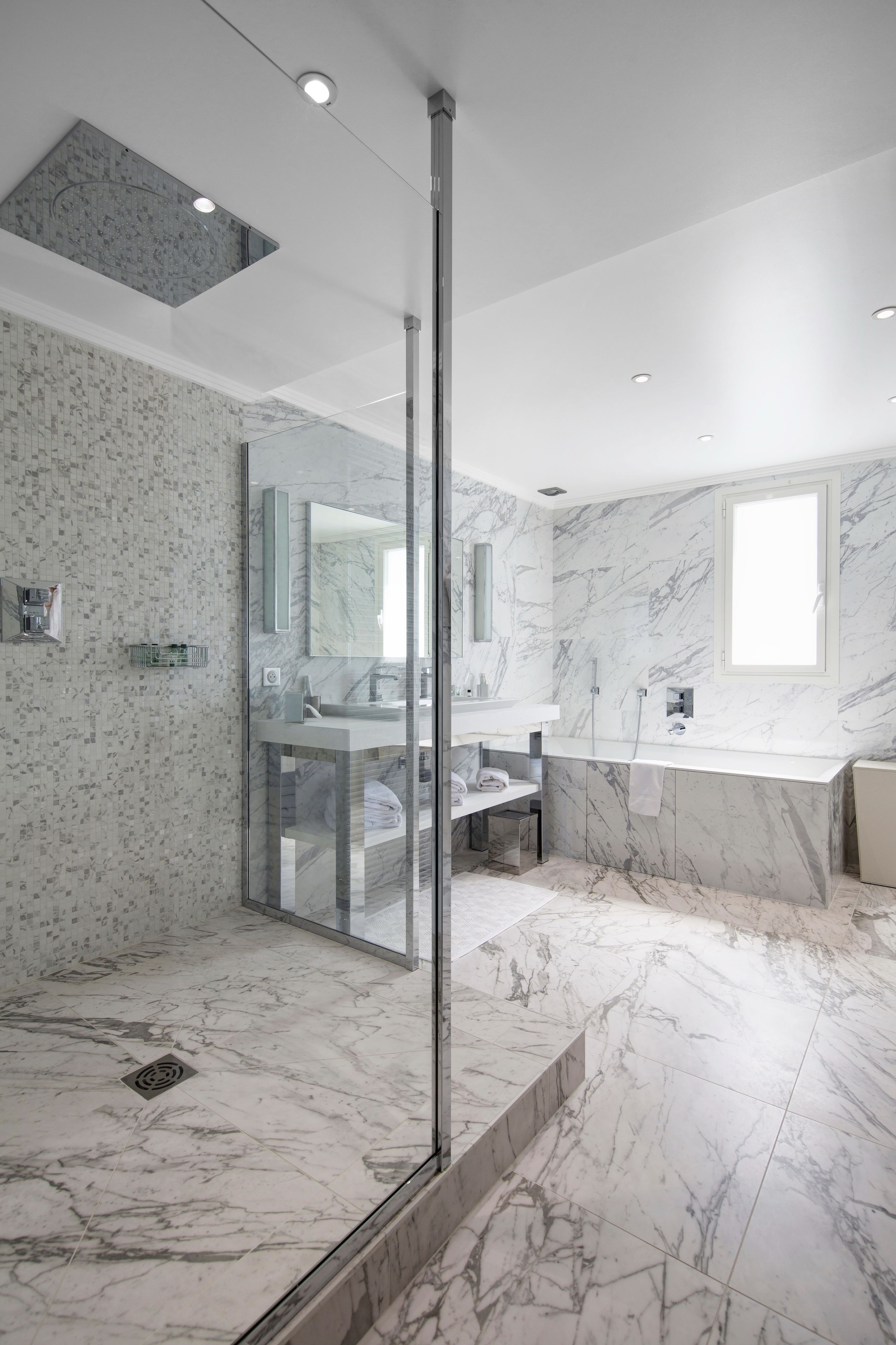 Une salle de bain moderne avec une douche à parois de verre, un sol en marbre et un grand miroir au-dessus du lavabo.