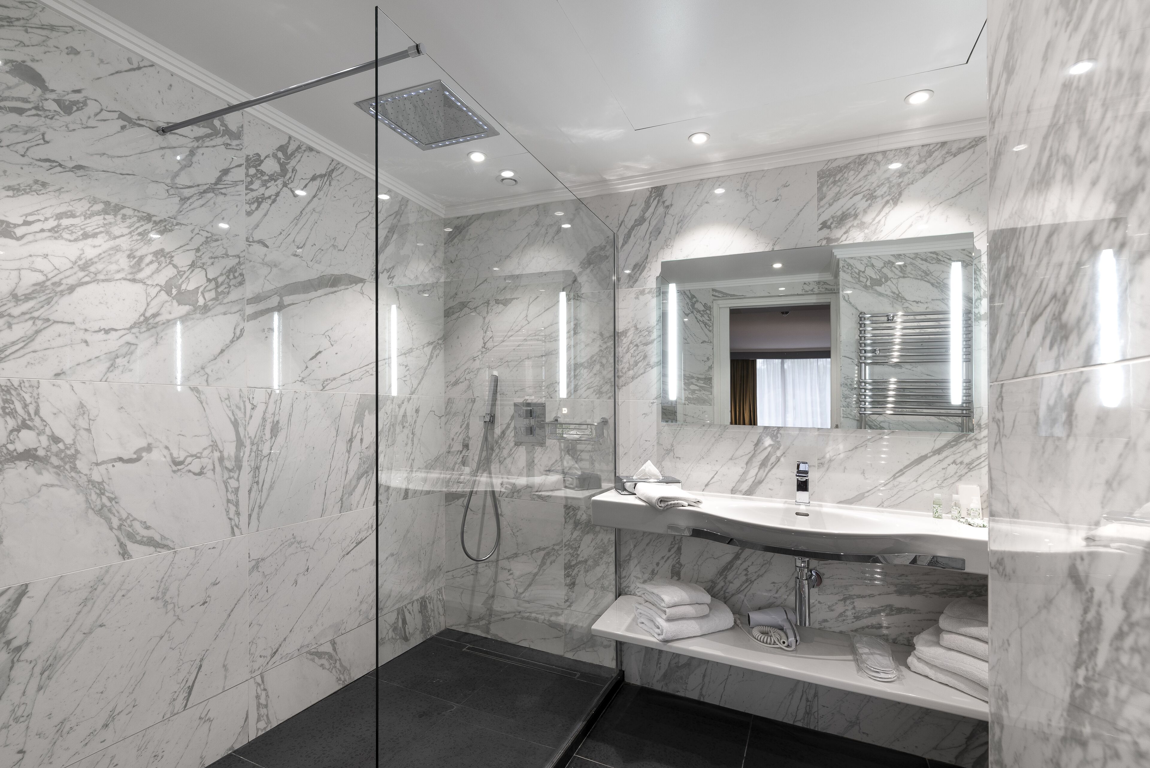 A modern bathroom with a glass-enclosed shower, a marble vanity, and a large mirror.