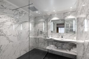 Un baño moderno con ducha de vidrio, tocador de mármol y un espejo grande.