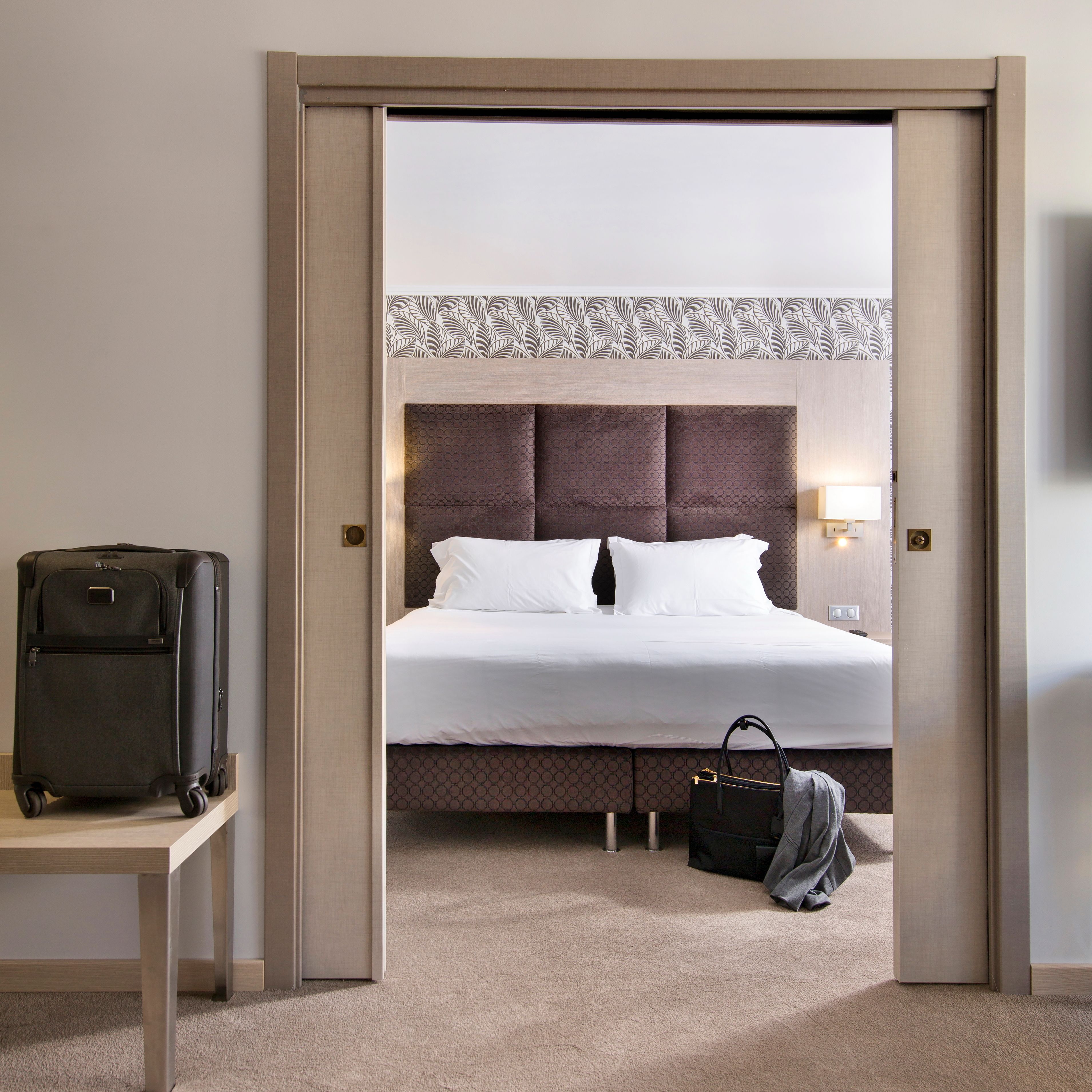 Une chambre d’hôtel avec un lit, une valise, un sac à main et une table.